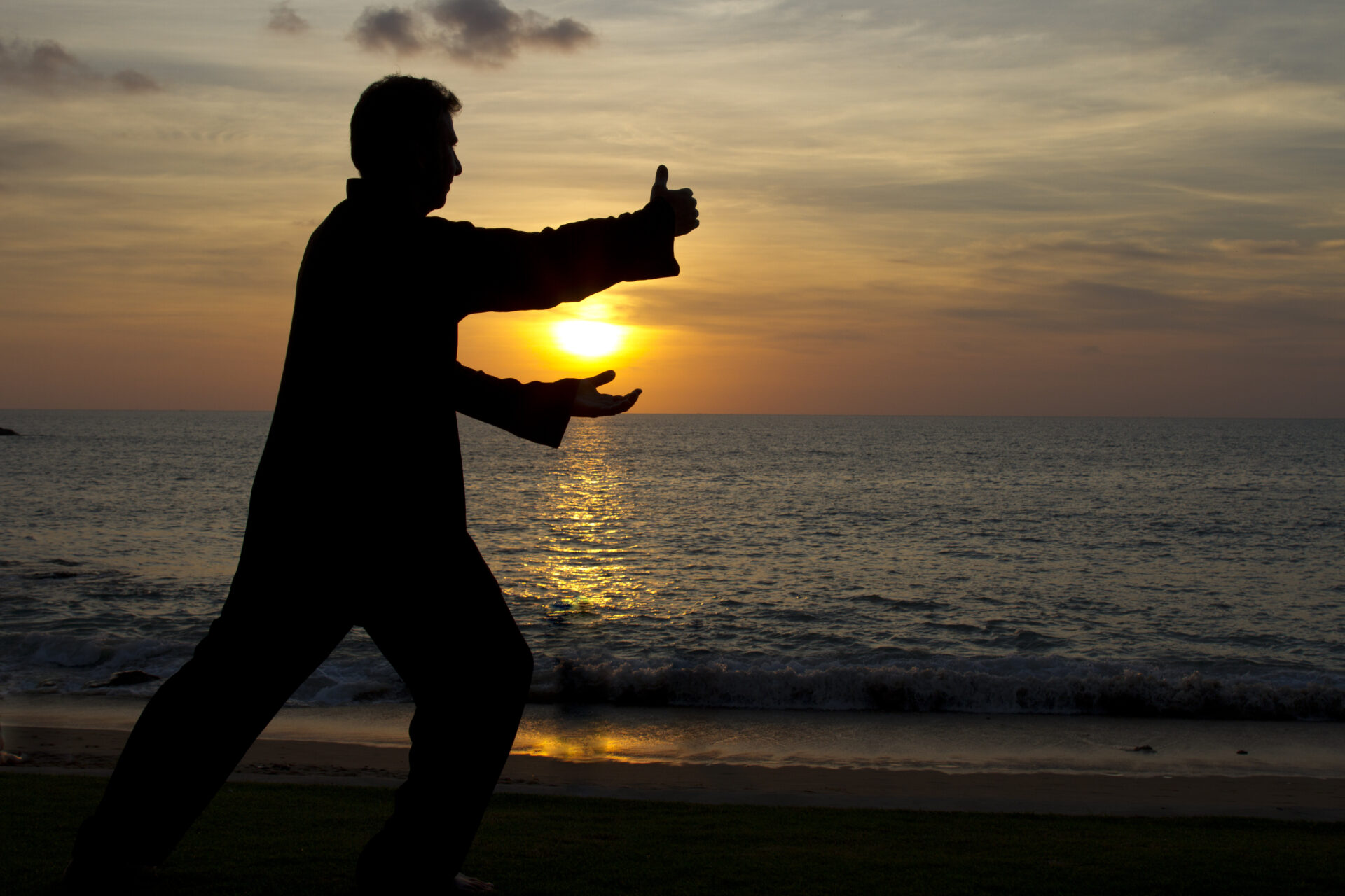 Silhouette of a man practicing Taiji with sunset background at the beach