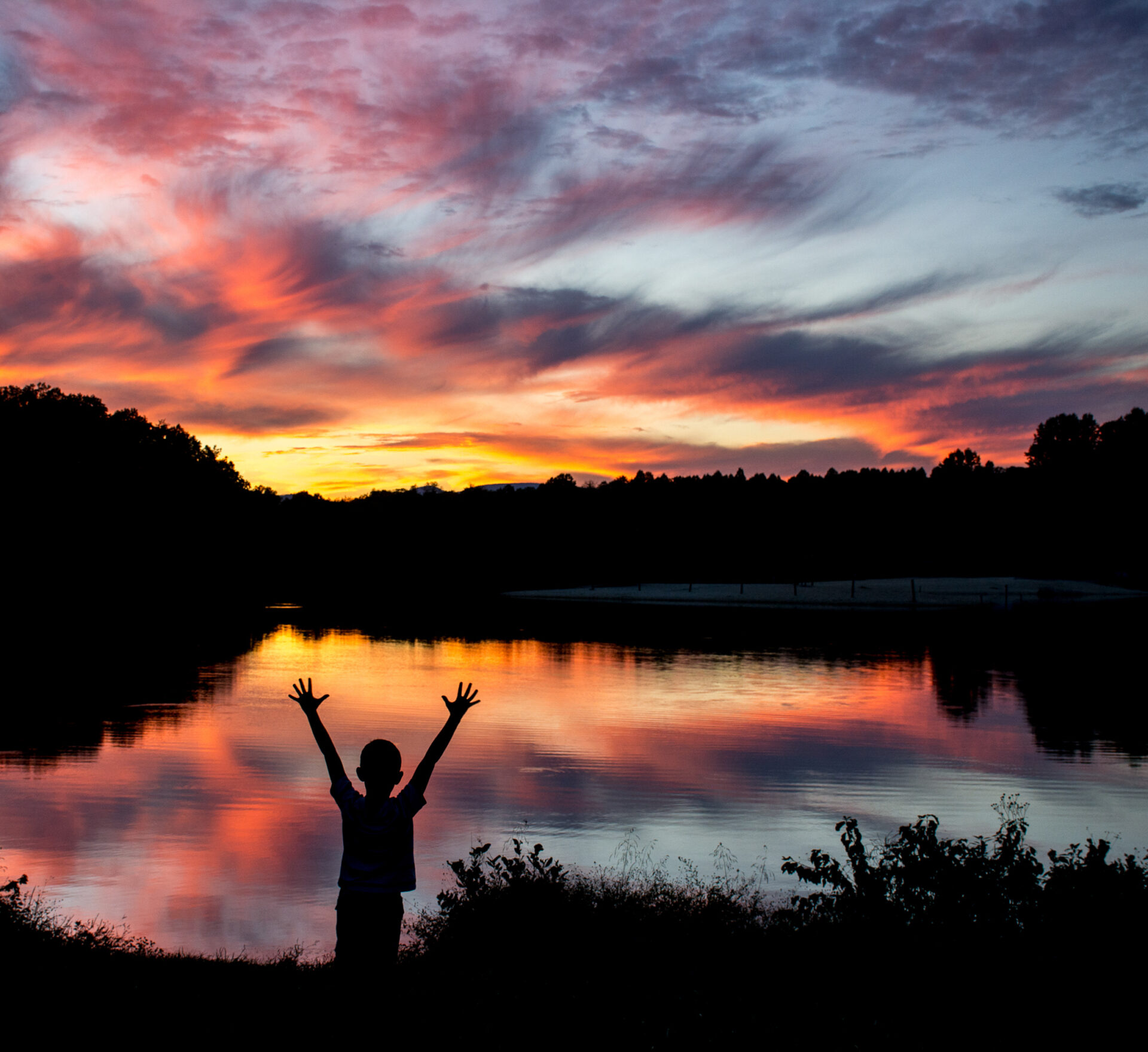 A boy enjoying a beautiful sunset at a lake.